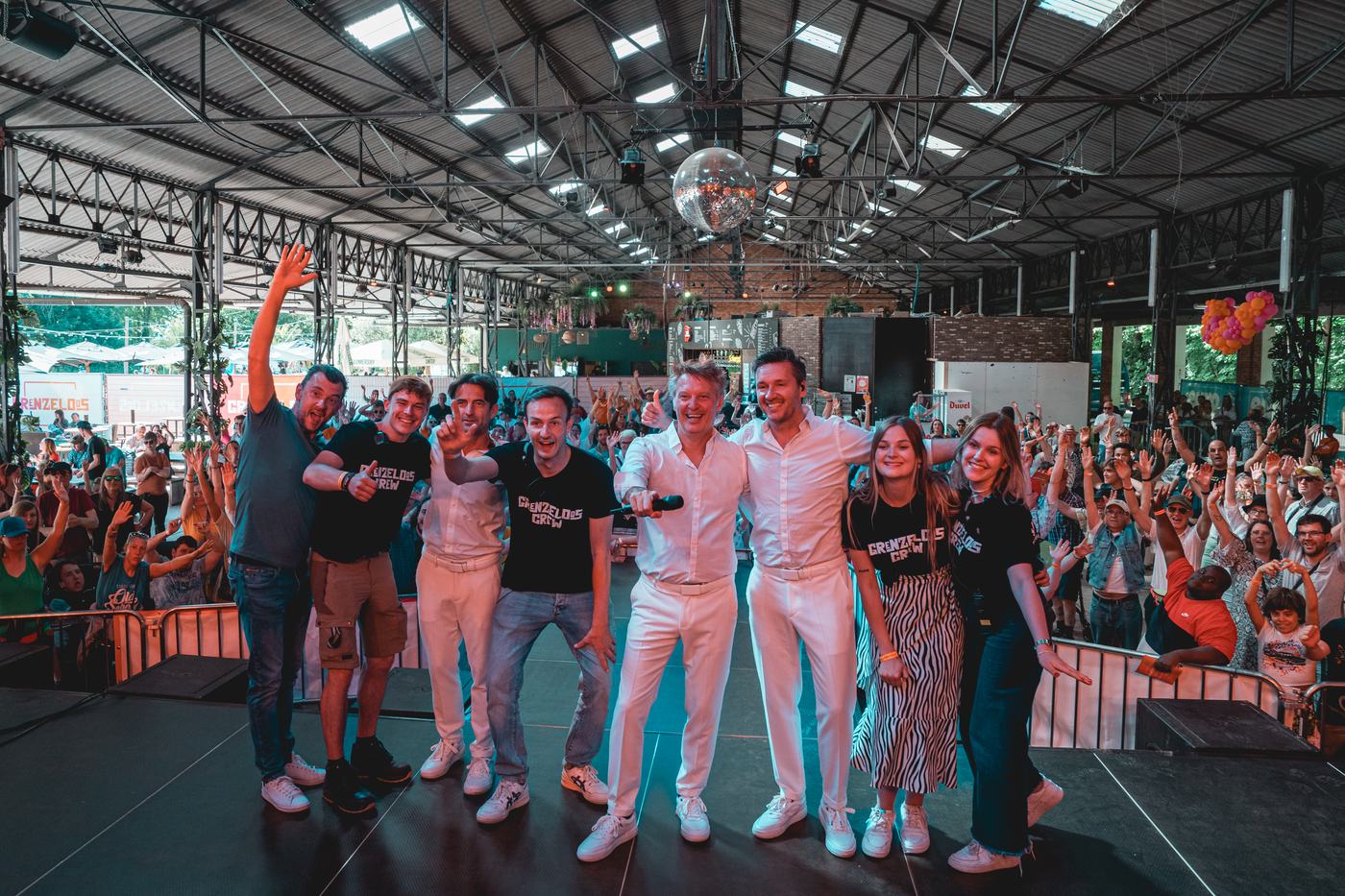 De Grenzeloos-crew op het podium, met een dansende massa op de achtergrond.