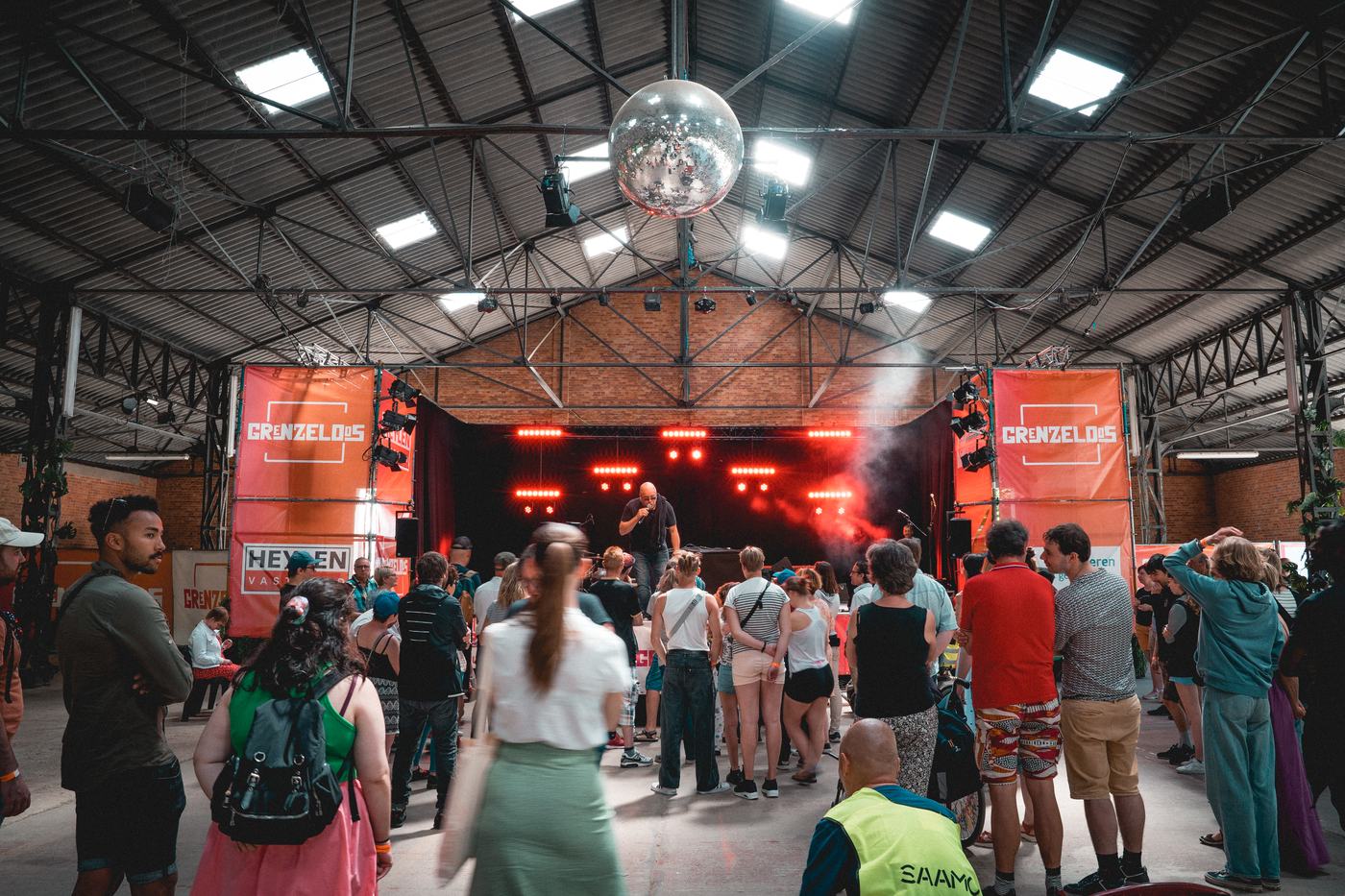 Een volle festivalhal met discobal en rode podiumverlichting.