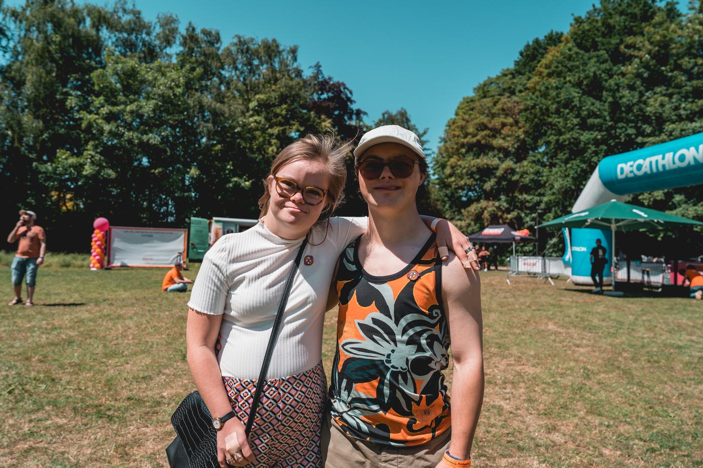 Twee bezoekers met de arm om elkaar heen genieten van een zonnige festivaldag.