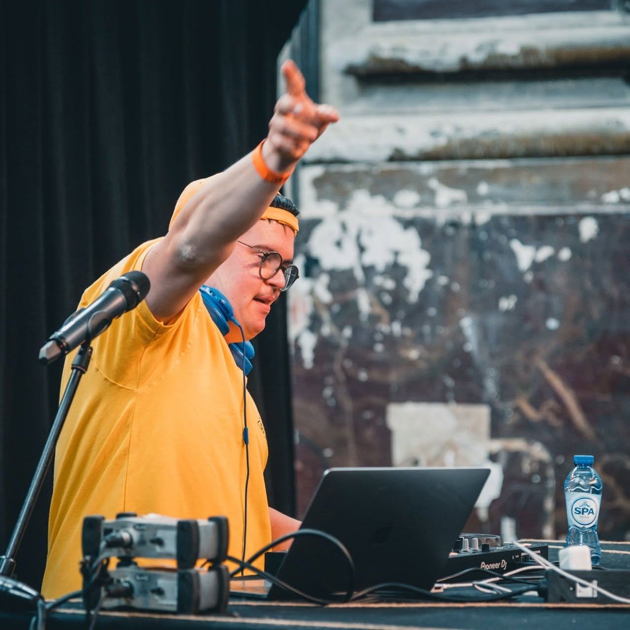 Een dj op het podium wijst enthousiast naar het publiek.