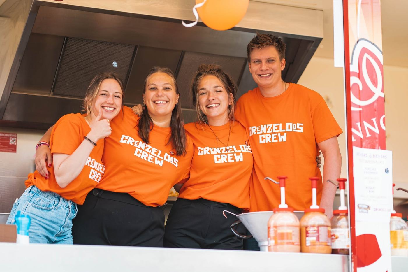 Vier vrijwilligers van de Grenzeloos Crew lachen samen bij de foodstand.