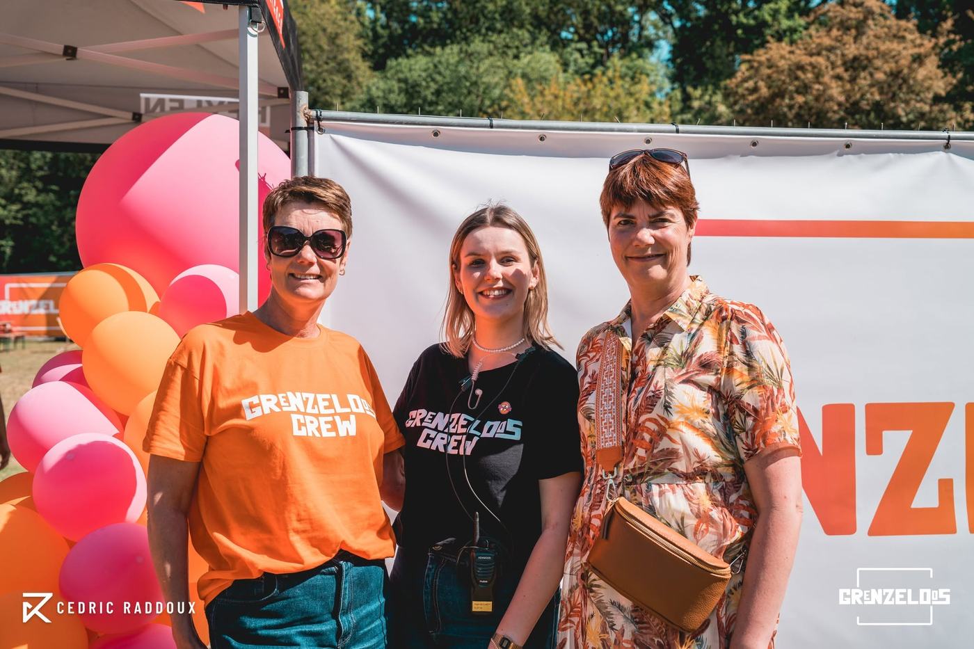 Drie leden van de Grenzeloos Crew poseren samen bij de ballonnendecoratie.